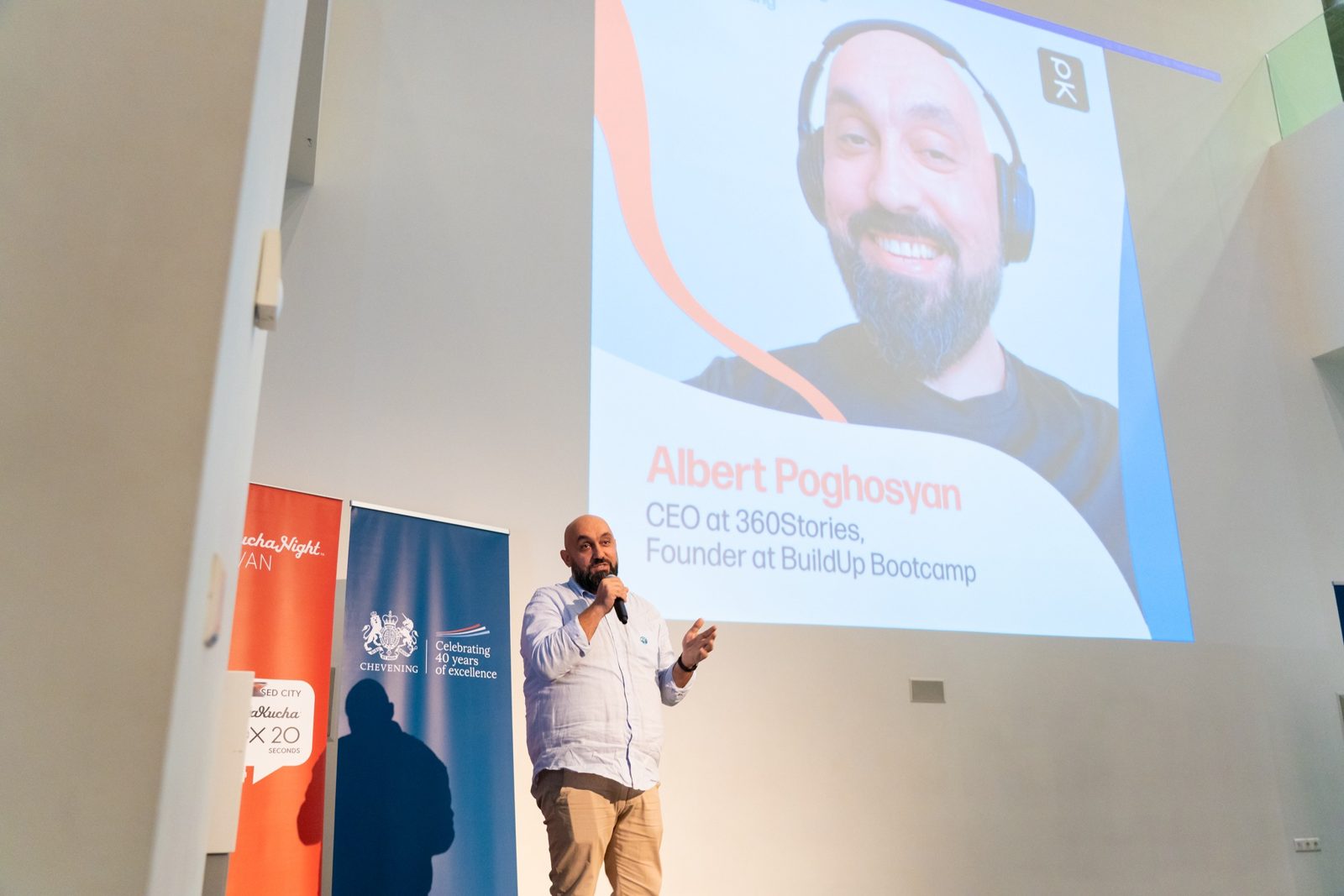 Albert Poghosyan speaking on stage, his speaker slide projected behind him